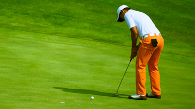 golfer in bright orange pants putting the ball into the hole